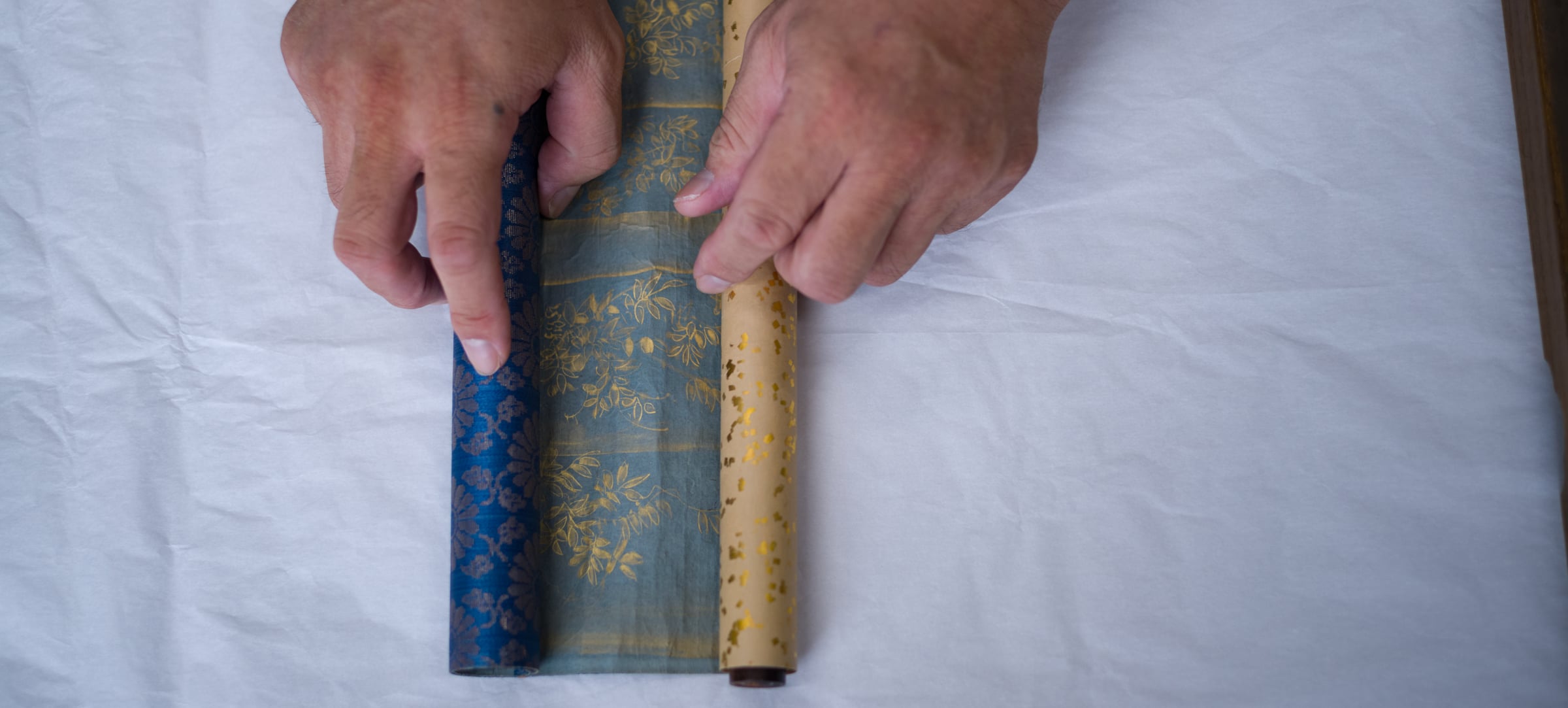 Hands holding two brocade-bound scrolls on white paper (photo: Takahiro Mitsui)