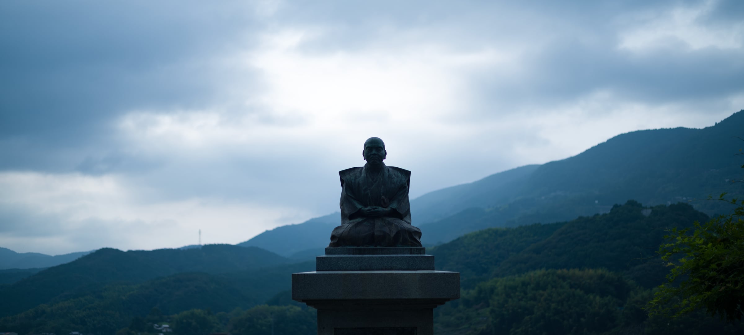 The silhouette of a seated bronze statue against mountains and a cloudy sky (photo: Takahiro Mitsui)