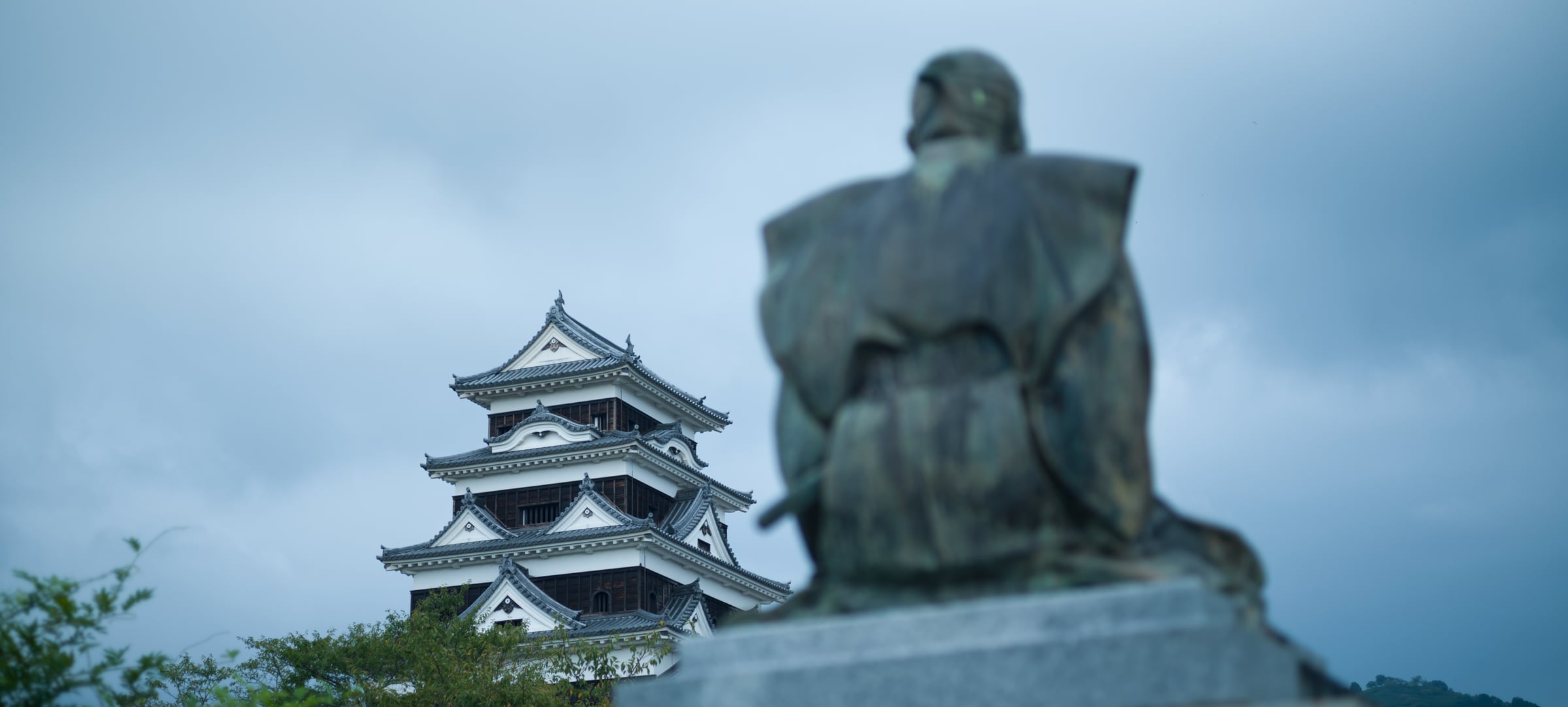 A bronze statue seen from behind, facing a white castle keep (photo: Takahiro Mitsui)