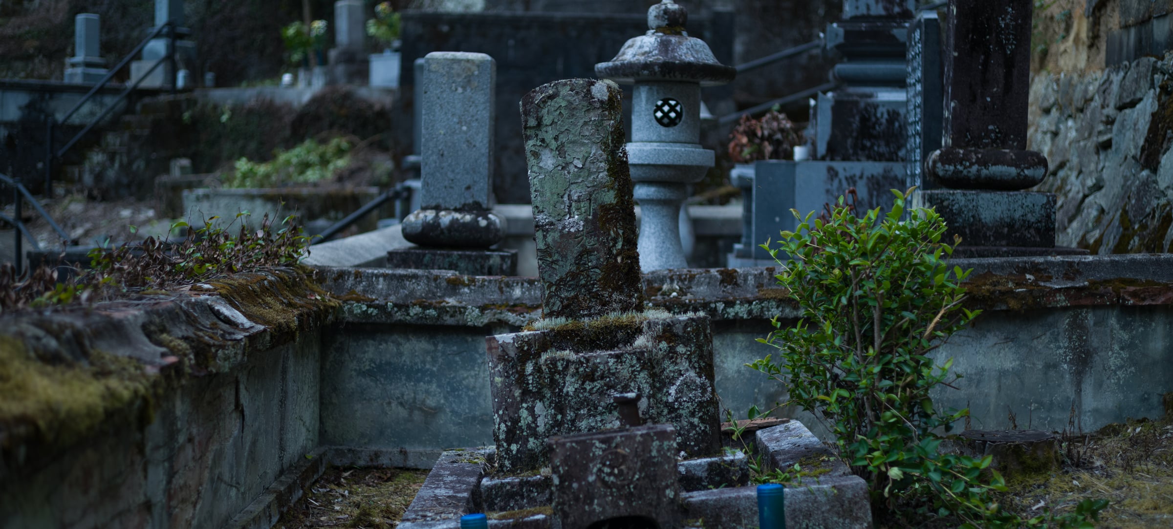 An old graveyard with a stone lantern and moss-covered gravestones (photo: Takahiro Mitsui)
