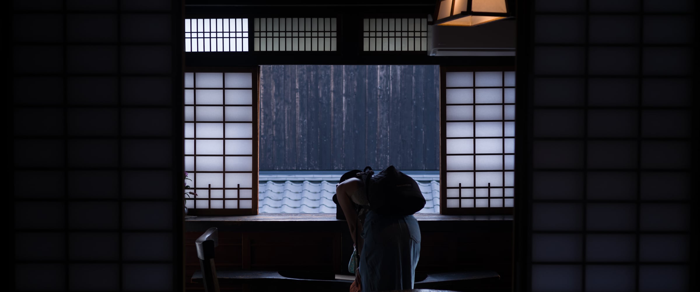 A figure bending by a window in a dark tatami room, backlit by paper shoji (photo: Takahiro Mitsui)