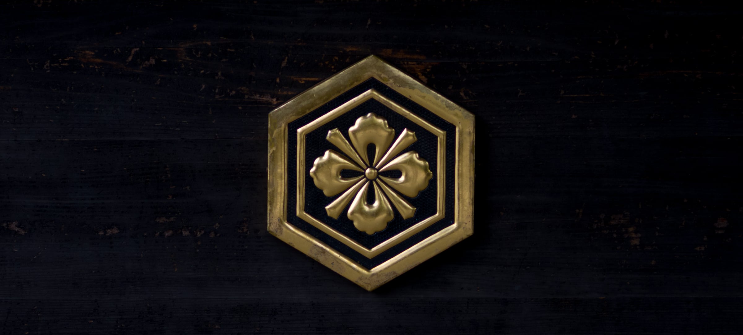 A brass crest of a flower within a hexagon, set against dark wood (photo: Takahiro Mitsui)
