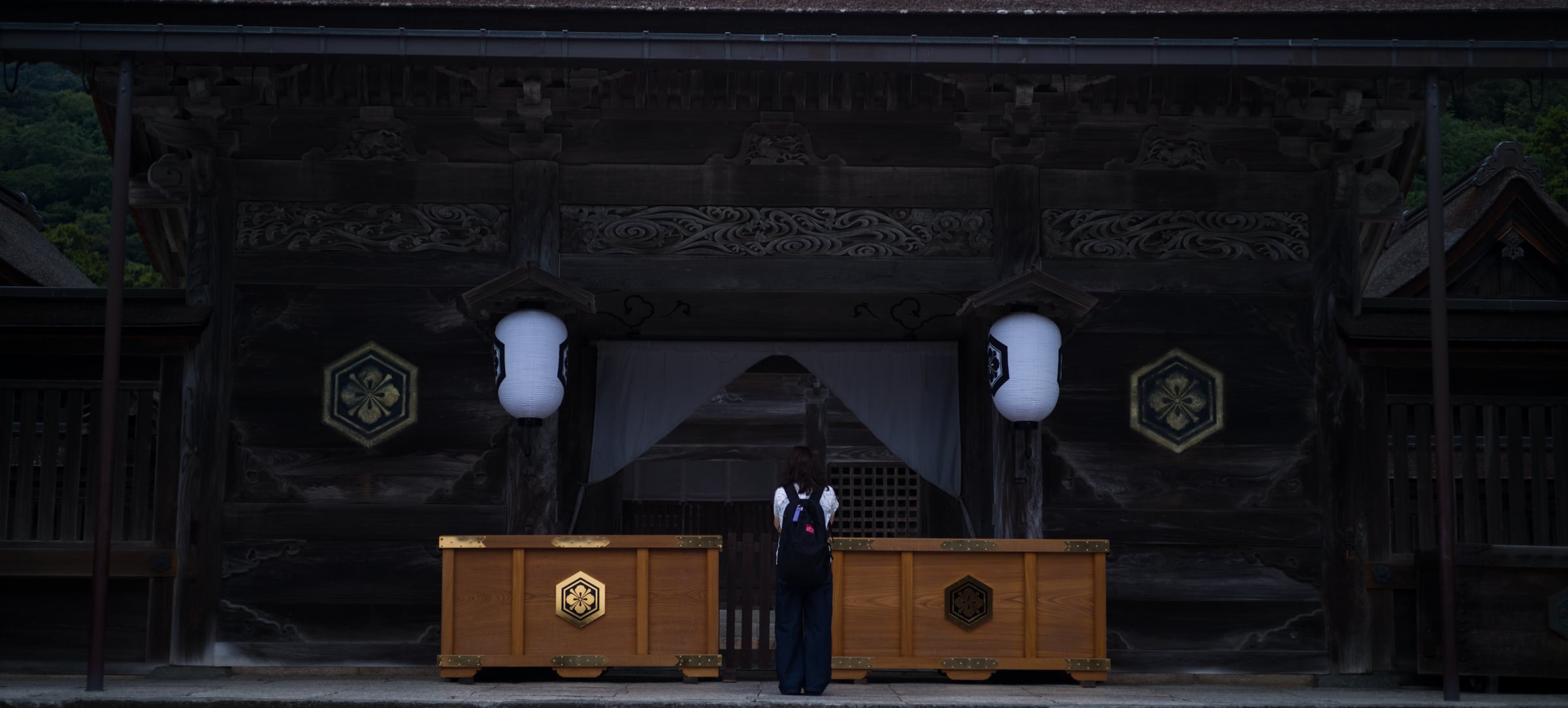 A woman praying alone before the offering boxes beneath white lanterns (photo: Takahiro Mitsui)