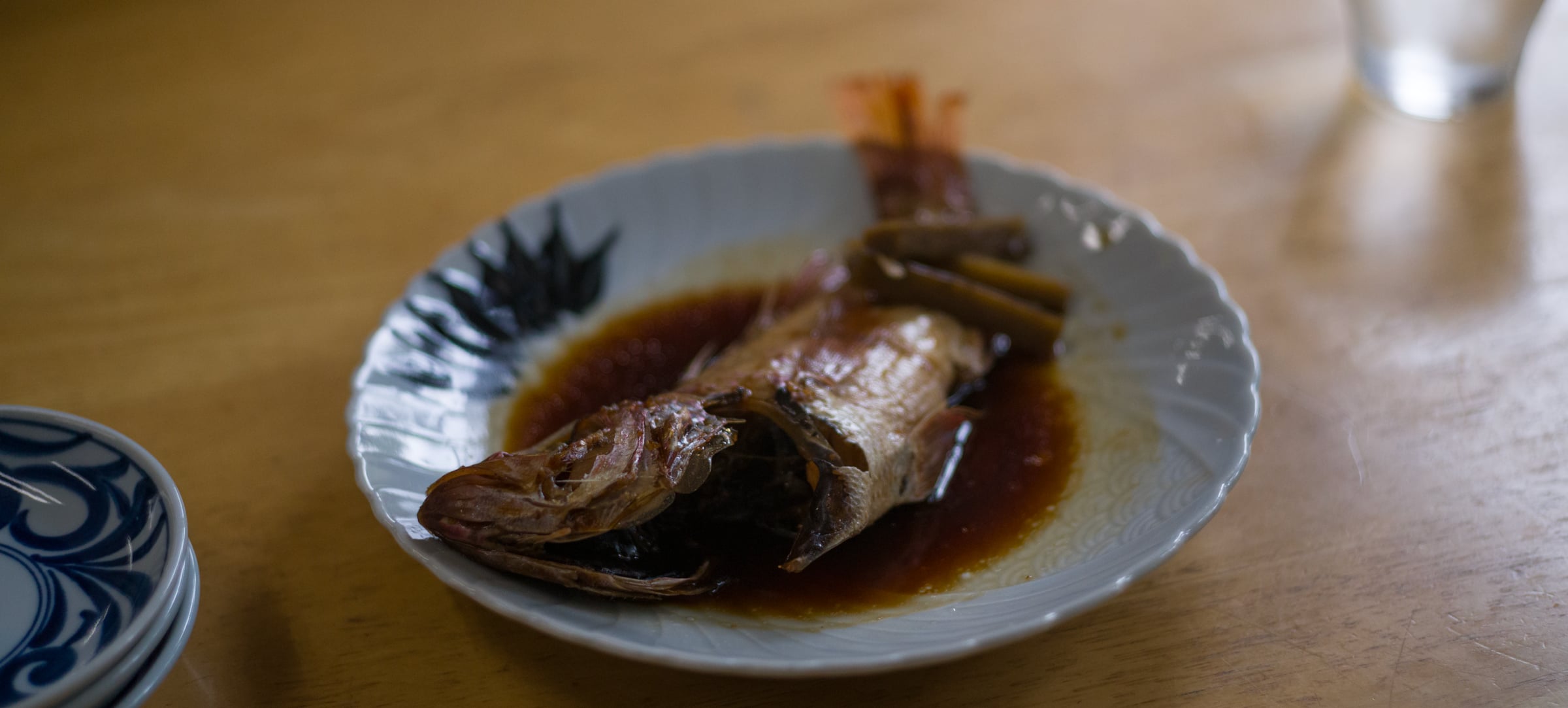 A simmered fish on a white plate in a pool of dark broth (photo: Takahiro Mitsui)