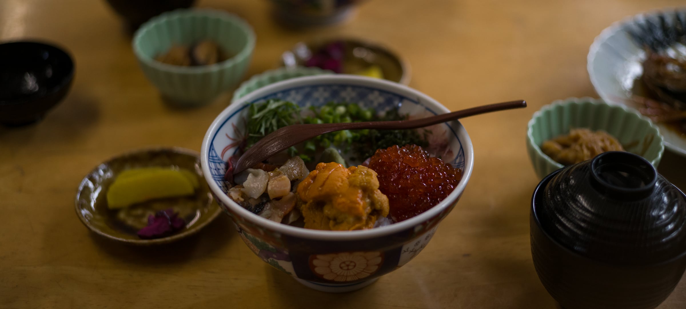 A bowl of rice topped with sea urchin, salmon roe and seafood, among small side dishes (photo: Takahiro Mitsui)